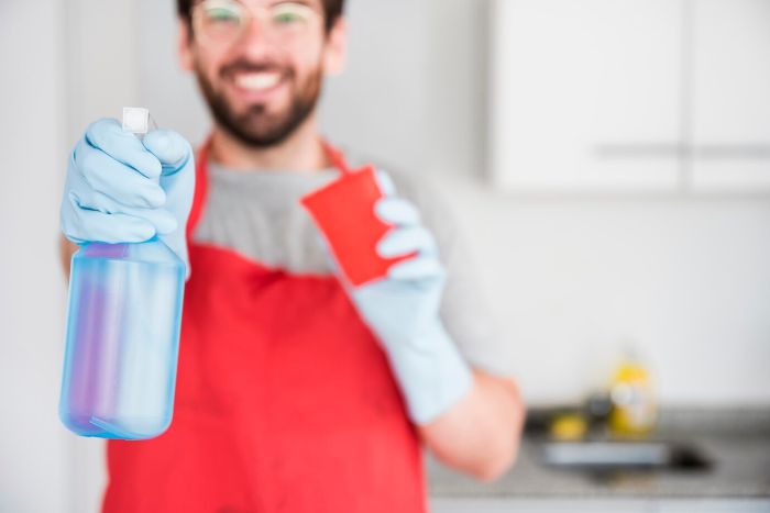 A person wearing gloves and holding a spray bottle and cloth, illustrating the concept of water-based cleaners as a safe cleaning option.