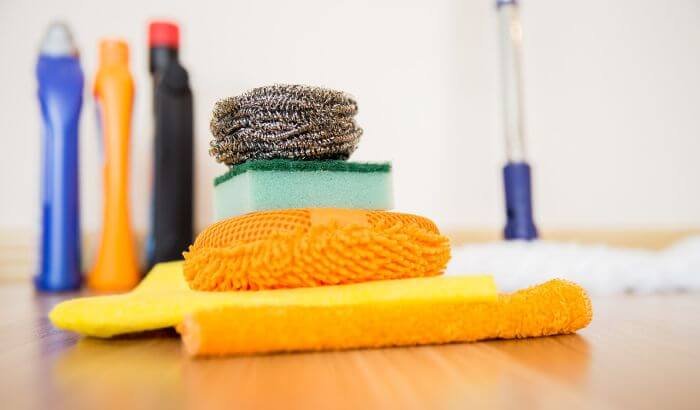 Cleaning supplies, including sponges, scrubbers, and cleaning liquids, neatly arranged on a wooden floor, highlighting the tools needed to avoid common mistakes during end of tenancy cleaning in London.