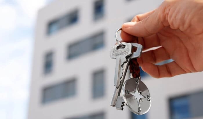 A hand holding keys in front of an apartment building, representing the importance of end of tenancy cleaning in property management.