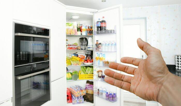 Hand pointing towards an open fridge filled with various food items, illustrating the process of cleaning a fridge without spoiling the food.