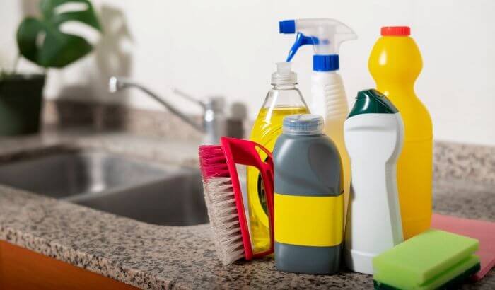 Various cleaning products and tools arranged on a kitchen counter, illustrating the importance of understanding ingredients and labels in cleaning products.