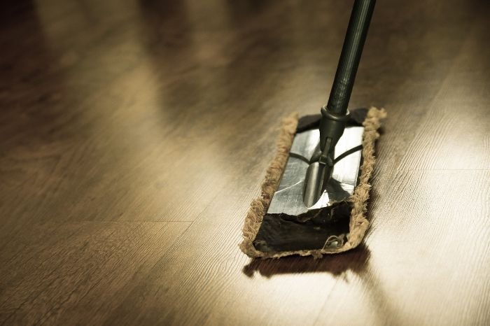A person mopping a wooden floor, emphasizing the importance of maintaining clean floors and surfaces for a neat and safe home environment.