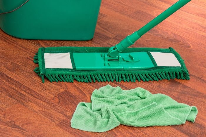 Green microfiber cloth and mop on a wooden floor, illustrating effective dusting methods using microfiber cloths.