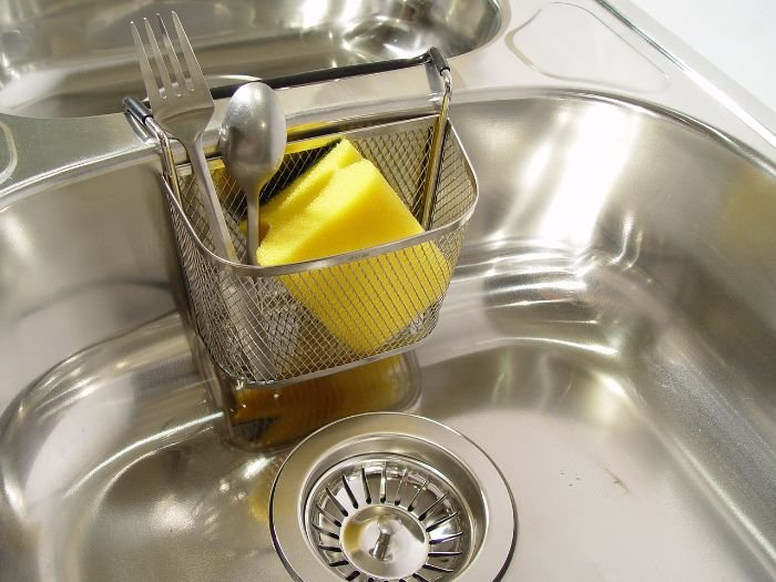 Clean stainless steel sink with utensils and a sponge, illustrating the use of a natural sink unblocker.