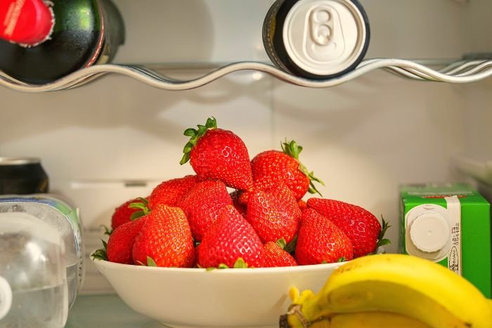 Fresh strawberries, bananas, and drinks arranged in a fridge, emphasizing safe practices for cleaning around food to prevent contamination.