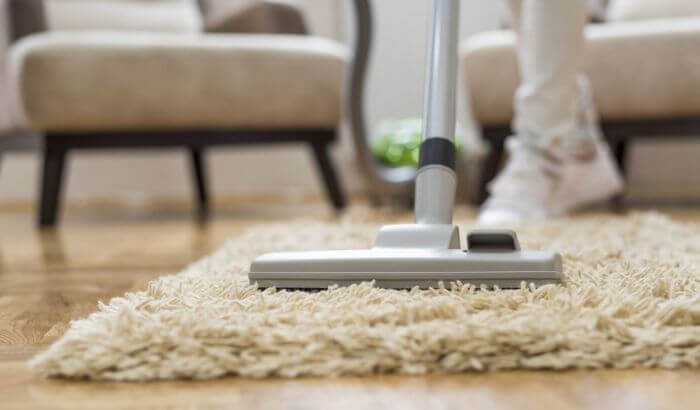 A person vacuuming a beige carpet, representing a quick and efficient 30-minute whole house cleanup strategy.