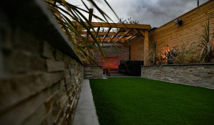 Modern landscaped garden in London with artificial grass, wooden pergola, and stylish lighting, showcasing top landscaping trends.