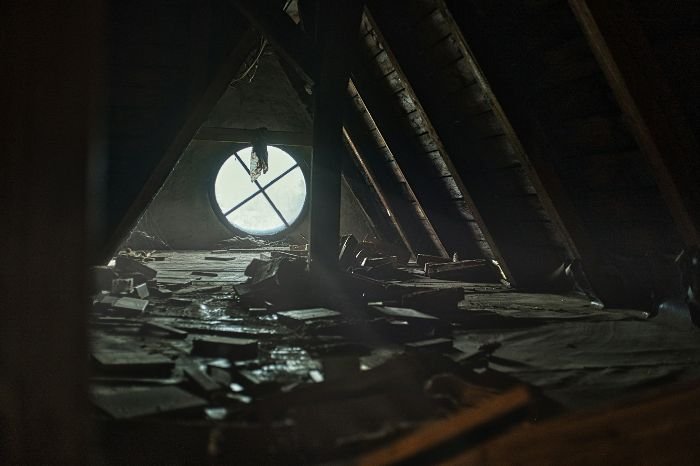 Dark attic interior with a round window, highlighting issues of mould and pests, emphasizing the importance of proper attic ventilation and maintenance