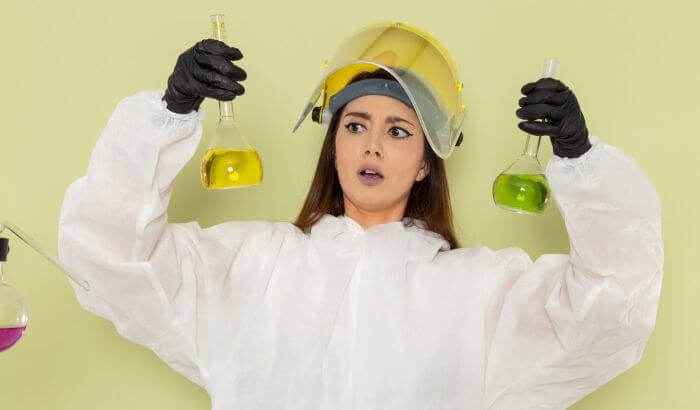 A person in protective gear holding two bottles of cleaning solutions, illustrating the importance of avoiding common household cleaning hazards to ensure safety during cleaning tasks.