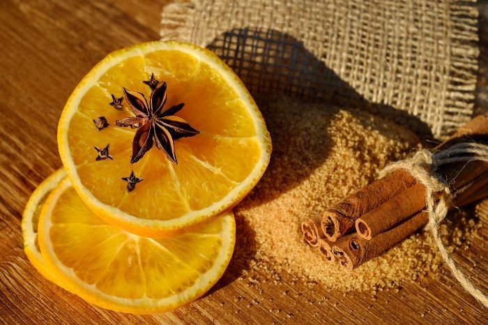 Slices of orange with cloves and star anise, paired with cinnamon sticks, symbolizing natural ingredients for making a baking soda and essential oil freshener.