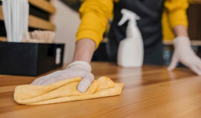 Person wearing gloves and using a yellow cloth to clean a wooden surface, highlighting health and safety practices in cleaning.