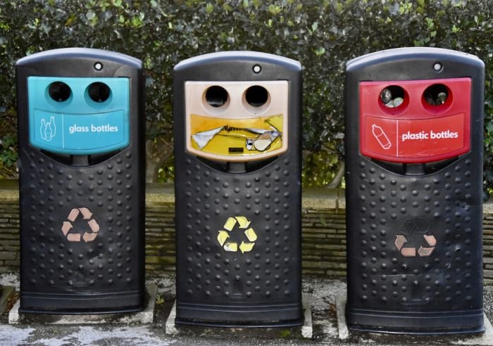 Recycling bins for glass, paper, and plastic, illustrating the benefits of sustainable waste management in promoting environmental health and business efficiency.