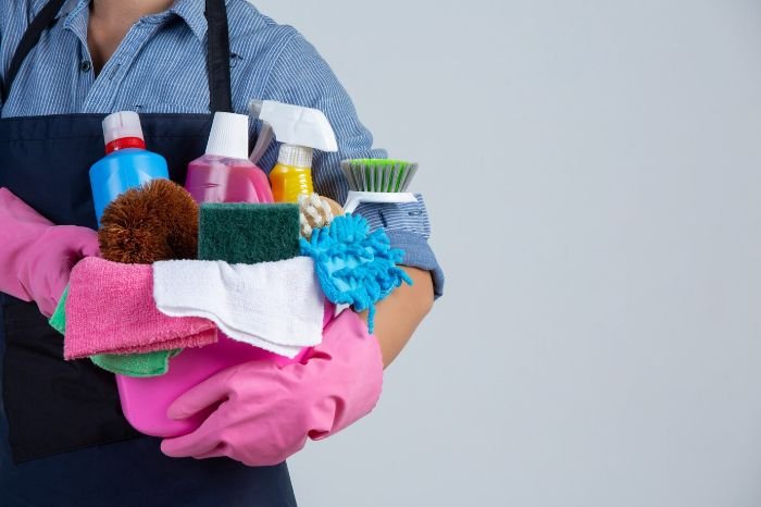 Person holding cleaning supplies for curtains and blinds, including brushes and detergents, emphasizing regular dust removal for a cleaner home