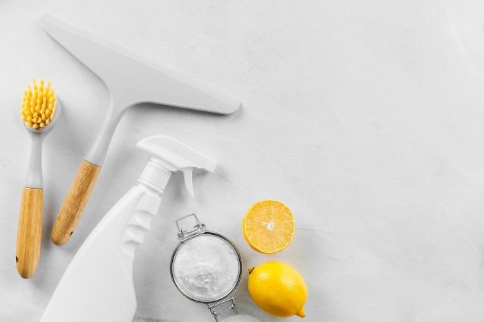 DIY citrus glass cleaner ingredients, including a spray bottle, brush, squeegee, baking soda, and fresh lemon, for a natural, streak-free shine on glass surfaces.