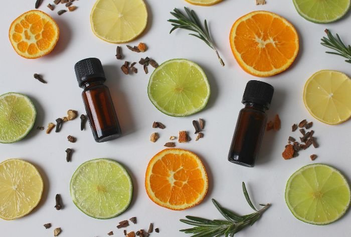 Essential oil bottles surrounded by slices of orange, lime, and lemon with rosemary and spices, emphasizing their use in natural cleaning