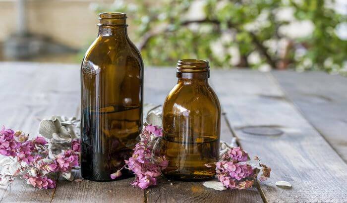 Amber bottles of essential oils surrounded by pink blossoms on a wooden table, representing their use in green cleaning
