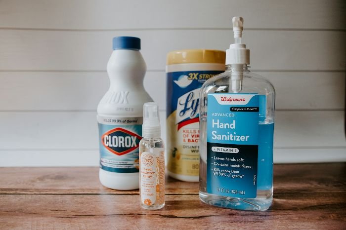 Assortment of common household cleaning products including Clorox, Lysol, and hand sanitizer on a wooden surface, emphasizing the importance of understanding cleaner ingredients