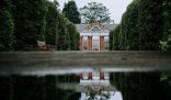 Beautiful garden pathway in London with reflective water, leading to a classic building, illustrating landscaping tips for London's unique climate.