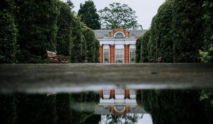 Beautiful garden pathway in London with reflective water, leading to a classic building, illustrating landscaping tips for London's unique climate.