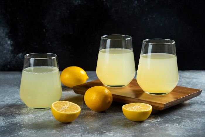 Glasses of fresh lemon juice surrounded by whole and sliced lemons, highlighting lemon juice as a natural and effective degreaser for homemade cleaning solutions.