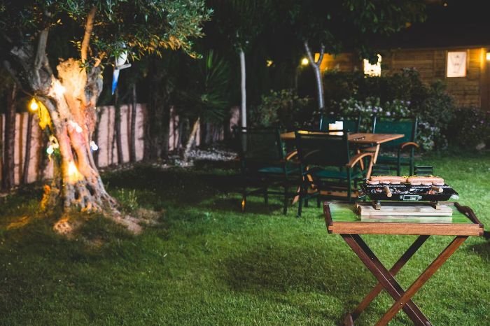 Outdoor garden at night with minimal lighting to protect nocturnal wildlife, featuring soft lights around a tree and a dining area.