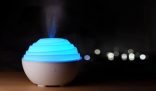 A blue-lit essential oil diffuser, a natural and child-safe air freshener, glowing softly in a dark room.