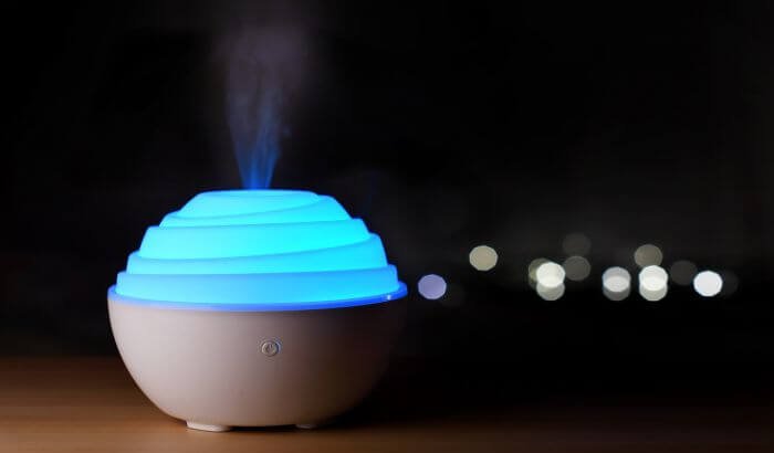 A blue-lit essential oil diffuser, a natural and child-safe air freshener, glowing softly in a dark room.