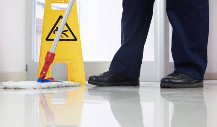 A person mopping the floor near a caution wet floor sign, demonstrating quick and easy floor cleaning techniques for safe and effective maintenance.