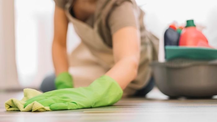 A person wearing green gloves scrubbing a floor to remove tough stains, with a bucket of cleaning supplies in the background, illustrating effective stain removal techniques.