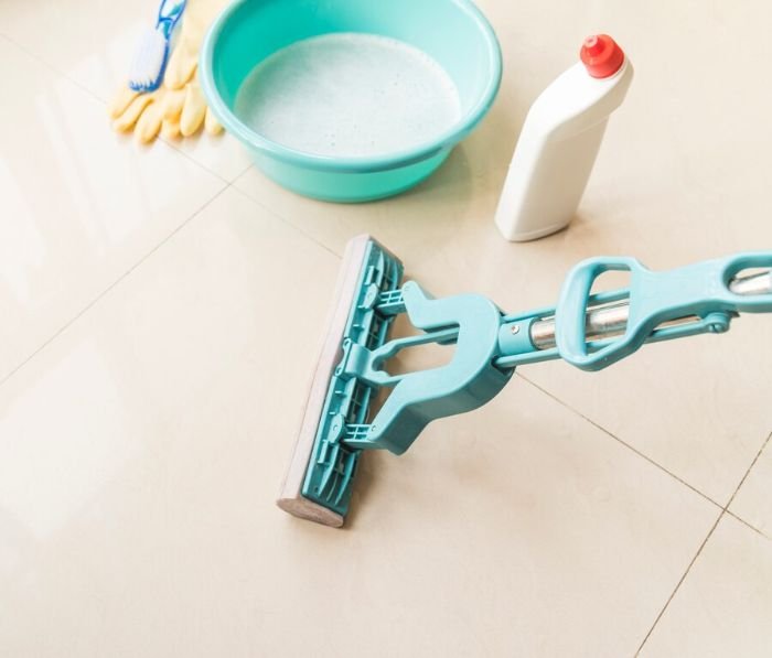 Cleaning equipment including a mop, bucket, gloves, and cleaning solution on a tiled floor, highlighting tips for avoiding slips, trips, and falls.