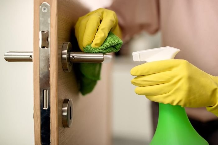 Person wearing yellow gloves cleaning a door handle with a cloth and multi-surface disinfectant spray for maximum effectiveness.