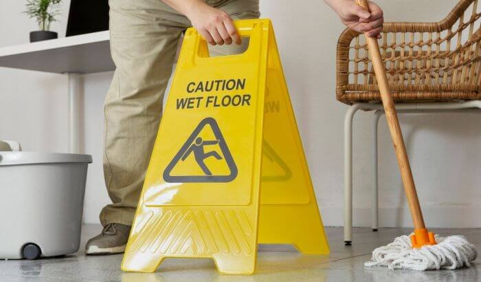 Person mopping next to a caution wet floor sign, illustrating best practices for achieving a spotless floor.