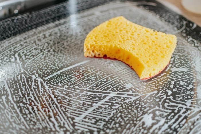 Yellow sponge on a soapy surface, demonstrating best practices for scrubbing, including keeping the sponge wet and rinsing often.