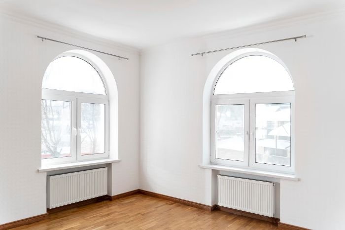 Bright room with clean radiators under arched windows, emphasizing the importance of cleaning and inspecting heating systems for efficient performance.