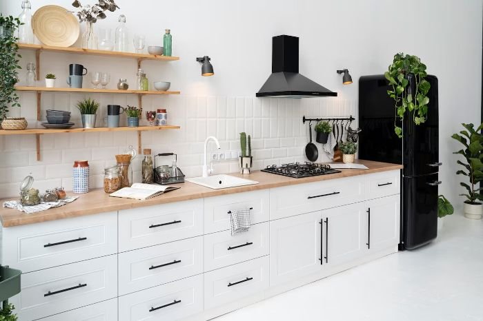 Modern kitchen with white cabinets, open shelves, and plants, highlighting the importance of detailed spring cleaning for a healthy and tidy kitchen.
