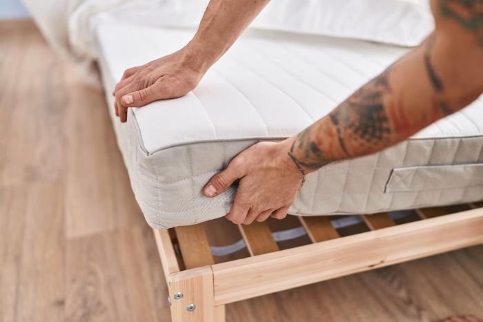 Person flipping a mattress on a wooden bed frame, emphasizing the importance of flipping and deep cleaning mattresses for better sleep and allergen control.
