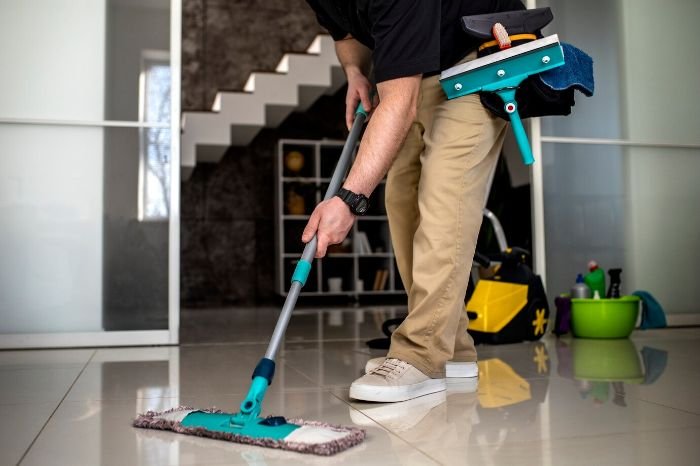 Person mopping a tile floor with cleaning supplies, illustrating how often to mop high-traffic and low-traffic areas.