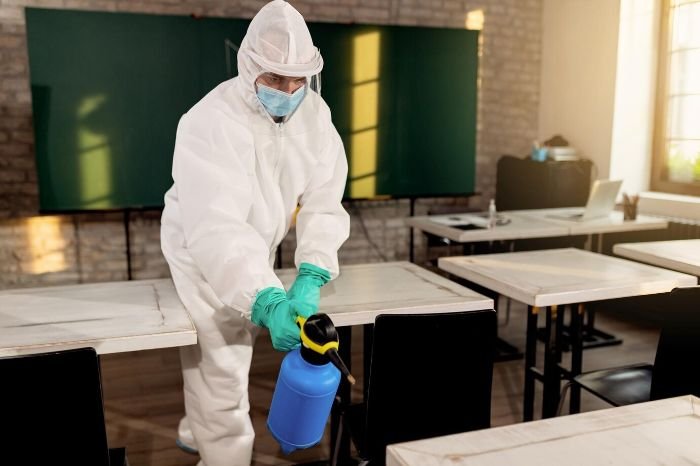 Person in protective gear disinfecting classroom surfaces with a powerful cleaning product, saving time and effort.