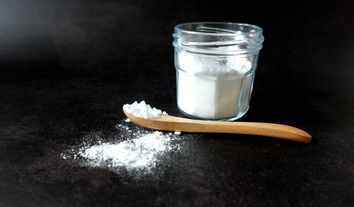Jar of baking soda with a wooden spoon, illustrating its use in cleaning.