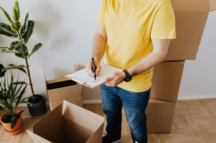 Person writing a cleaning checklist while organizing boxes, ensuring a thorough and organized end of tenancy cleaning process.