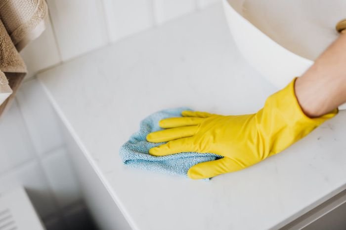 Person wearing yellow gloves disinfecting a surface with a blue cloth to prevent illness and maintain a clean, healthy home.