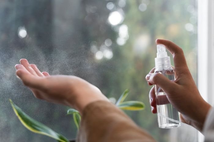 Person spraying DIY essential oil cleaning spray for cleaning various surfaces, made with water, vinegar, and essential oils like lemon or eucalyptus.