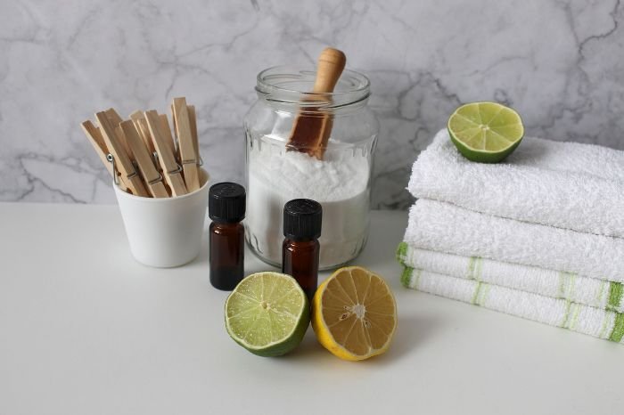 Eco-friendly cleaning setup with natural disinfecting ingredients including baking soda, essential oils, and citrus, arranged alongside towels and clothespins.