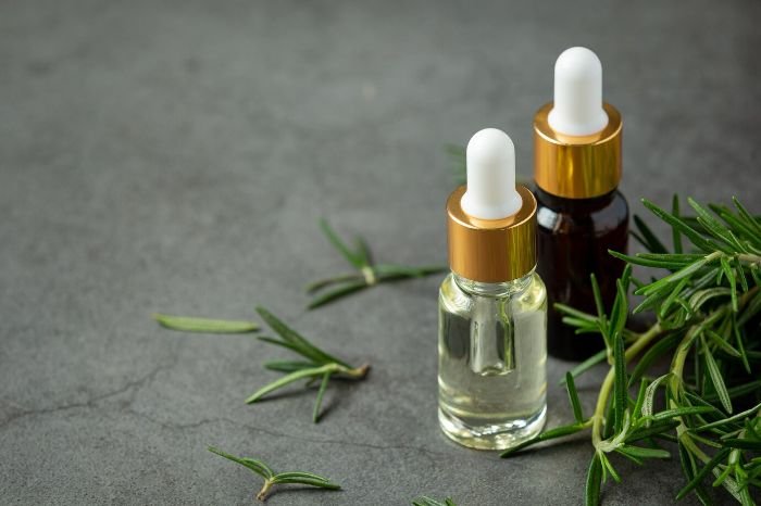 Bottles of eucalyptus, peppermint, and rosemary essential oils with fresh rosemary sprigs, used for natural home cleaning.