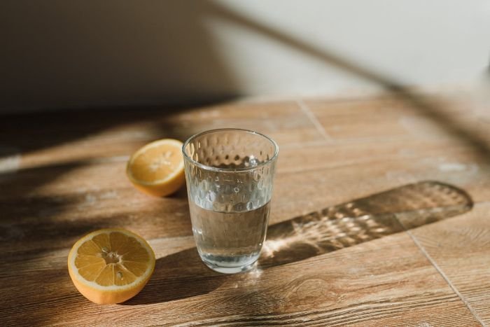 Glass of water with fresh lemon halves used for preparing a lemon juice and vinegar cleaning solution for multi-surface cleaning.