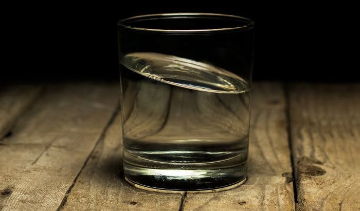 Glass of water on a wooden surface, symbolizing the importance of lowering water usage in eco-friendly green cleaning practices.