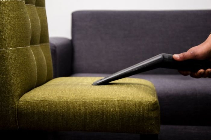 Tenant using a vacuum cleaner on a green chair to minimize wear and tear in a rental property through regular cleaning and maintenance.