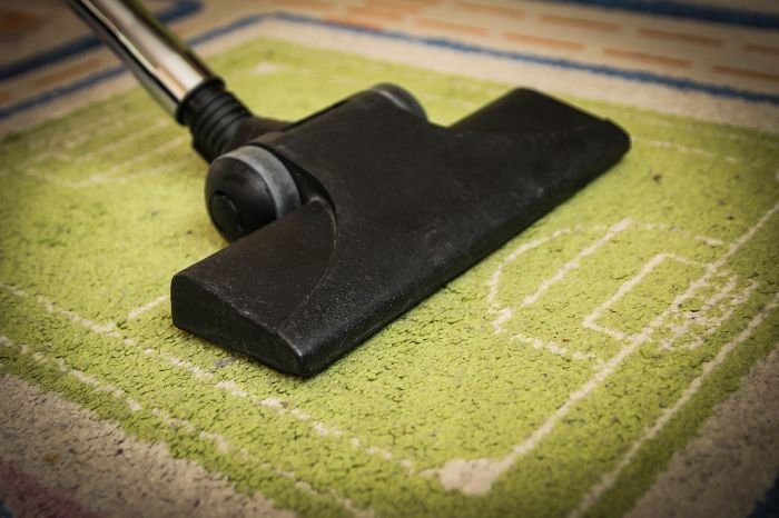 Vacuuming a green carpet with a vacuum head, demonstrating proper techniques for different surfaces such as carpets, rugs, hardwood, and tile floors.