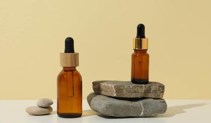 Essential oils in amber glass bottles displayed on stacked stones, used for effective natural cleaning solutions.