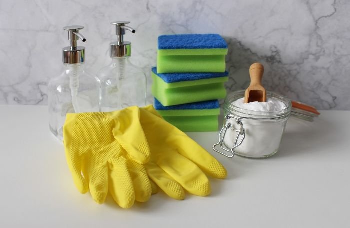 Cleaning supplies including white vinegar, baking soda, sponges, and rubber gloves for natural cleaning solutions.